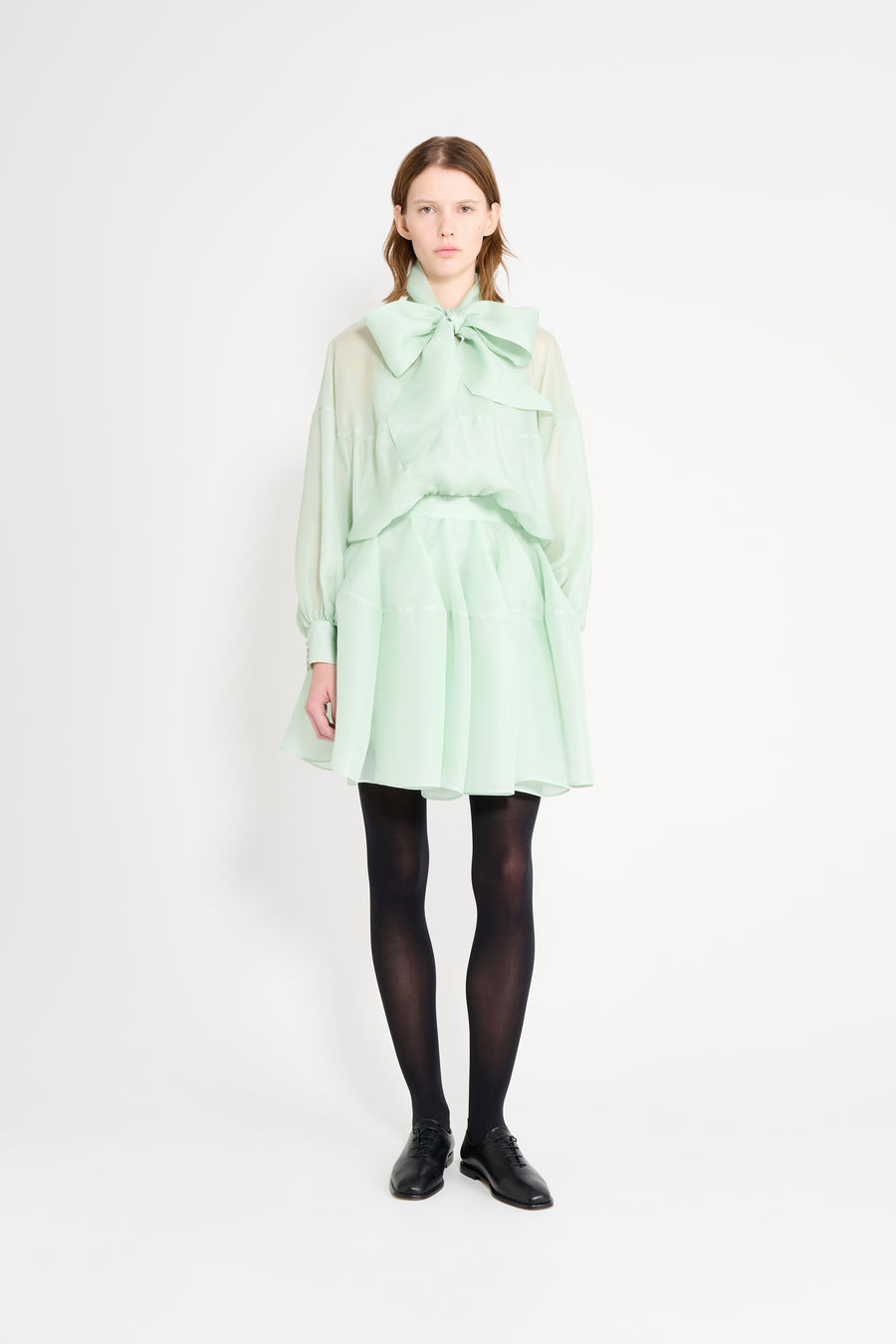 Person wearing a light green dress with a large bow on a white background