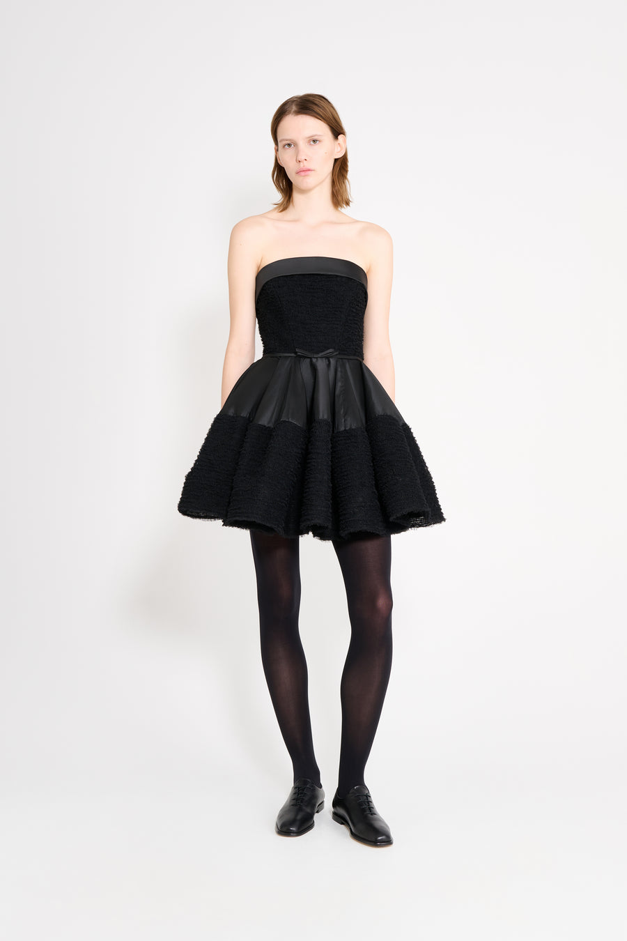 Woman wearing a black strapless dress with a flared skirt on a white background