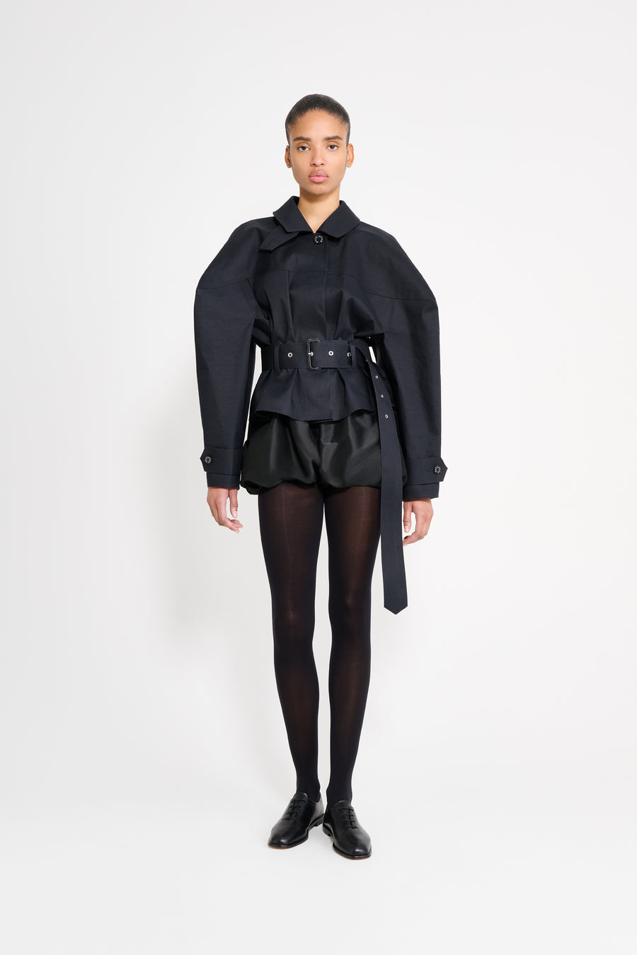 Person wearing a black outfit with a coat and skirt on a white background