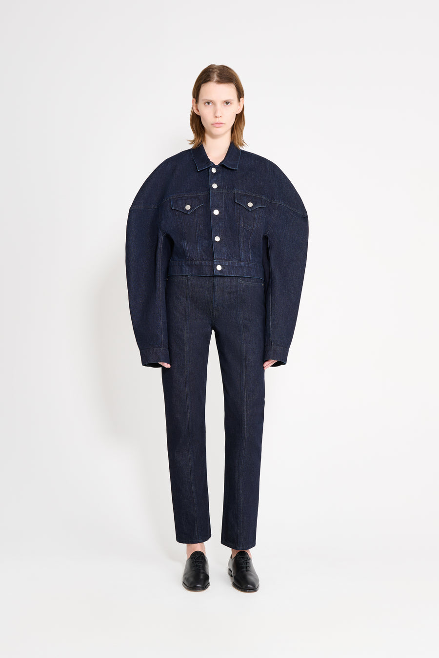 Person wearing a dark denim jacket and pants on a white background
