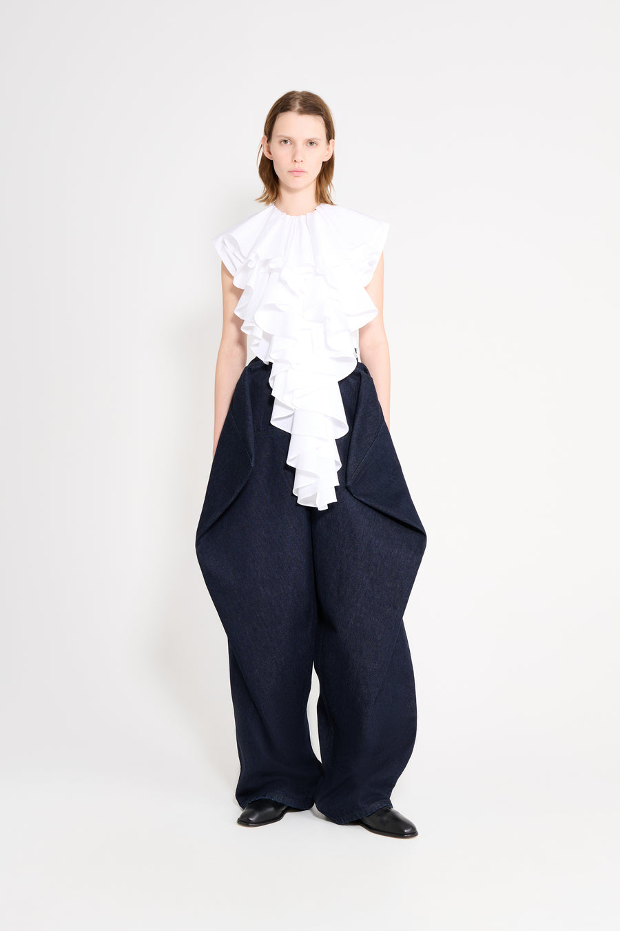 Person wearing a white ruffled top and navy wide-leg pants on a white background