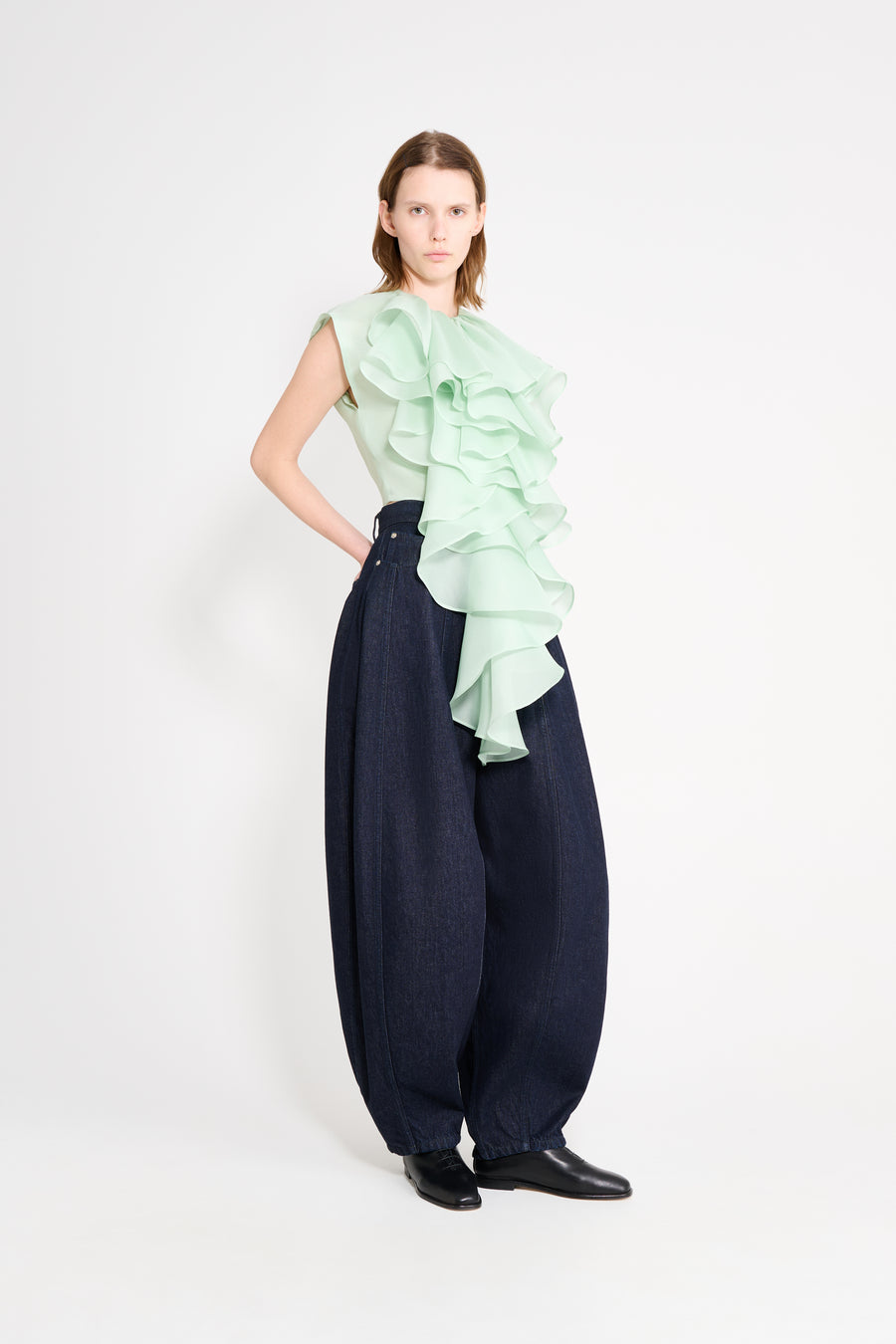 Woman wearing a light green ruffled top and navy wide-leg pants on a white background
