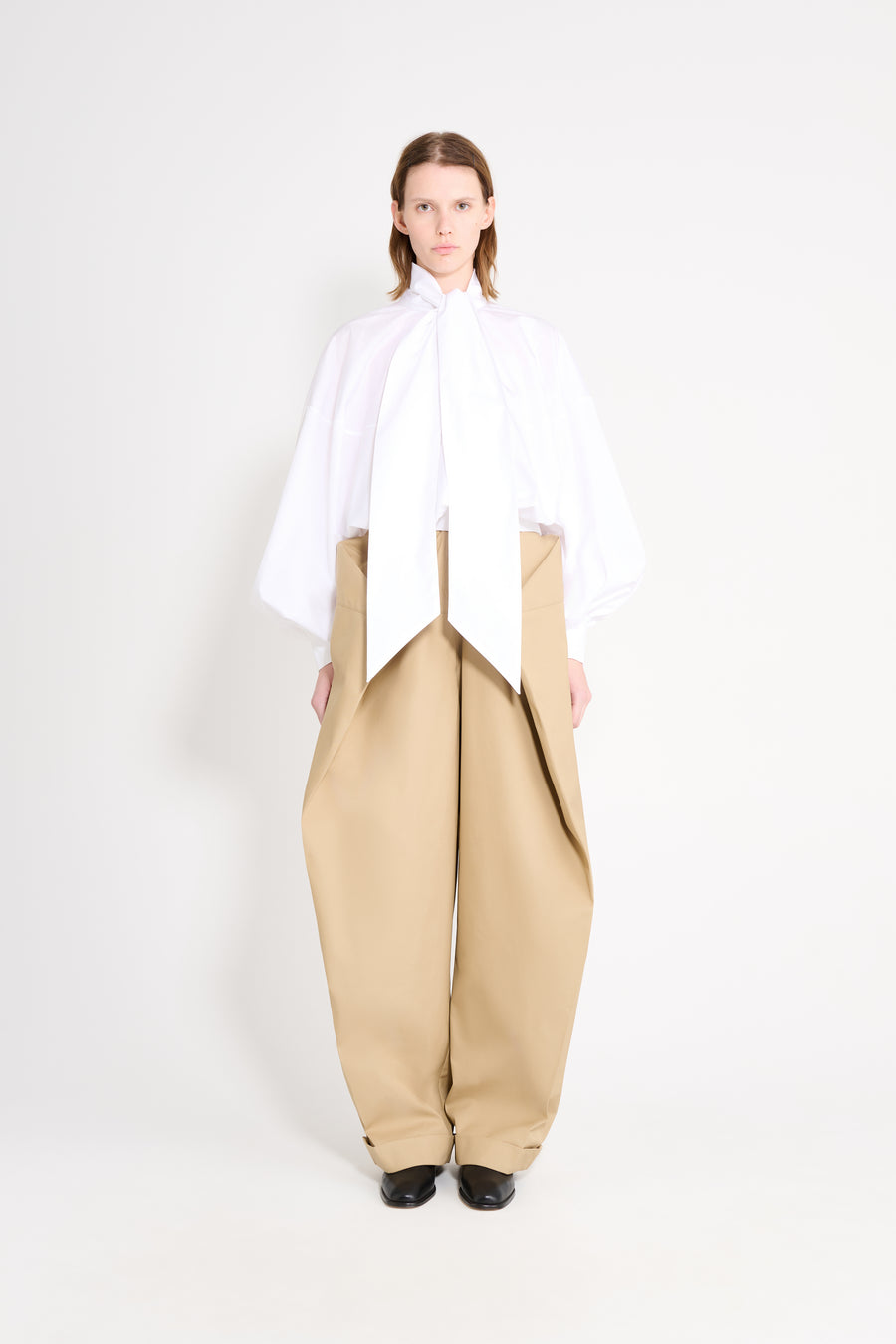 Model wearing a white blouse with beige pants.