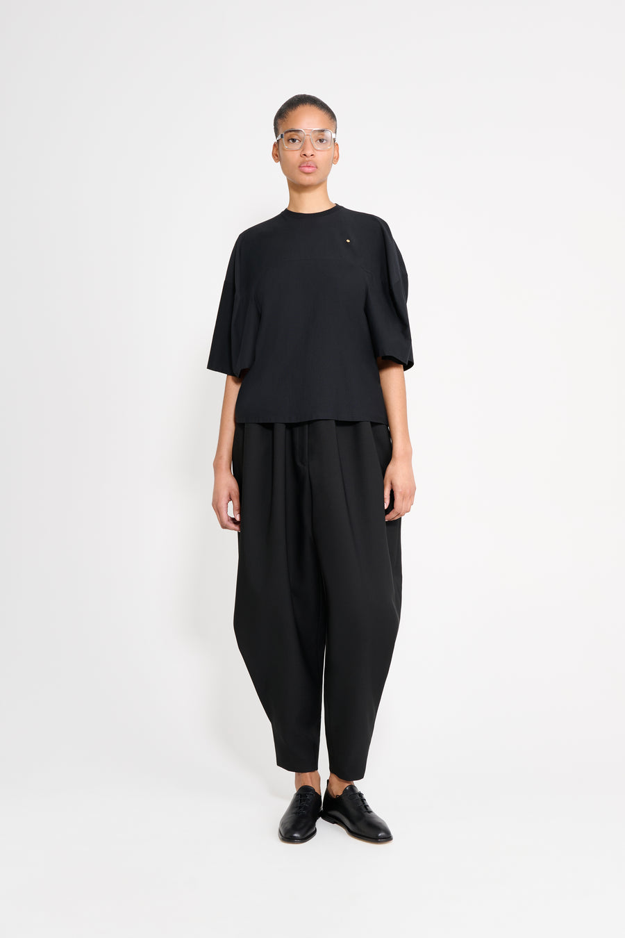 Model wearing a black t-shirt with black trousers on a white background.