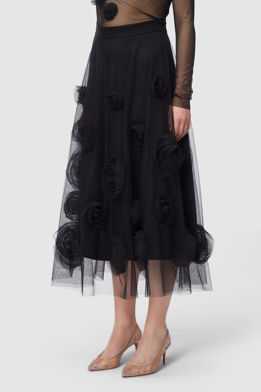 Black tulle skirt adorned with layered organza floral appliqués, paired with a sheer mesh top and embellished heels.