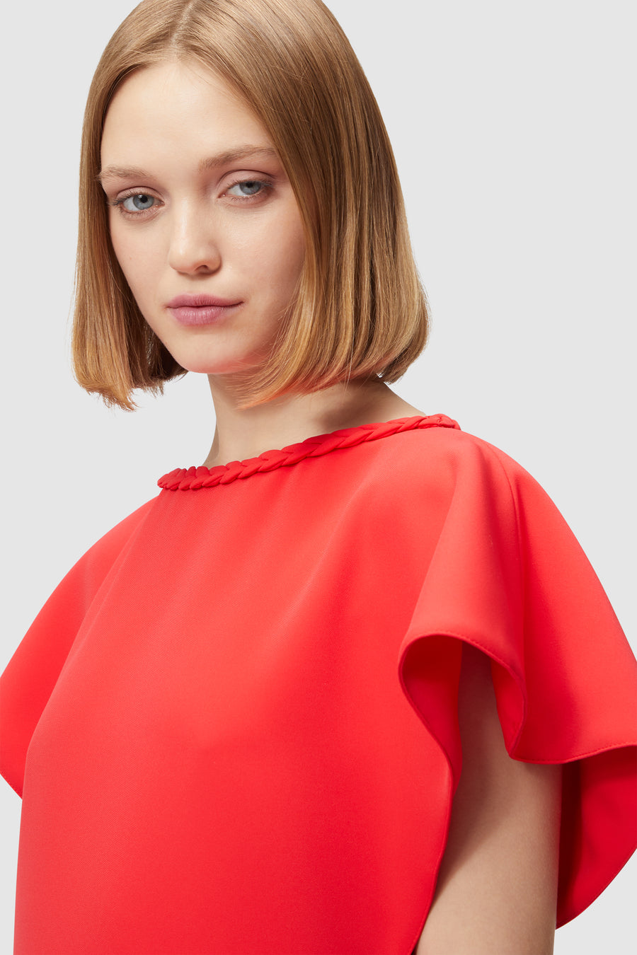 Elegant red dress with a braided neckline, featuring soft, flowing sleeves and a sleek silhouette, set against a neutral background.