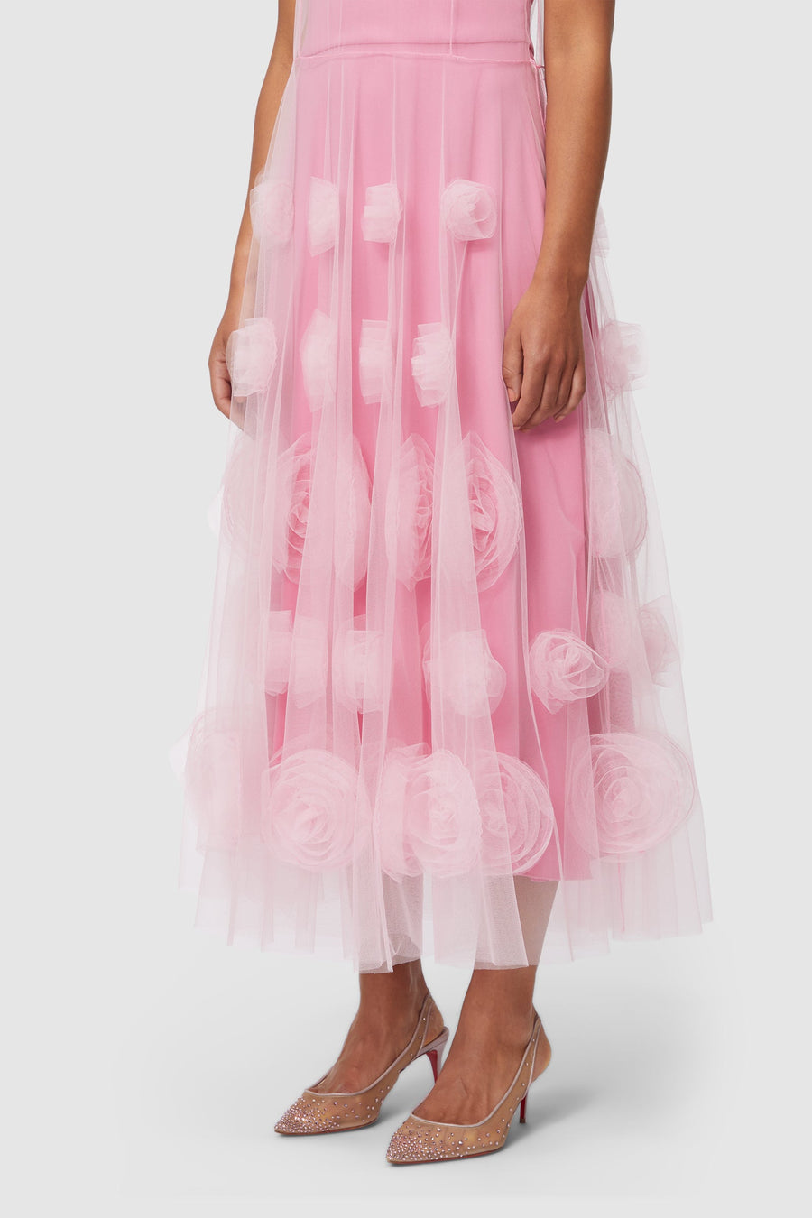 Pink dress with layered tulle featuring 3D floral appliqués, paired with sparkling, transparent heels.