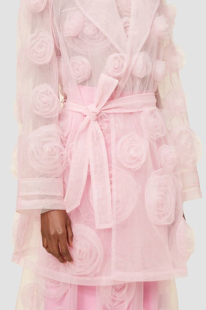 Pink sheer tulle trench coat adorned with delicate rosette appliqués and waist-defining tie belt for an elegant look.