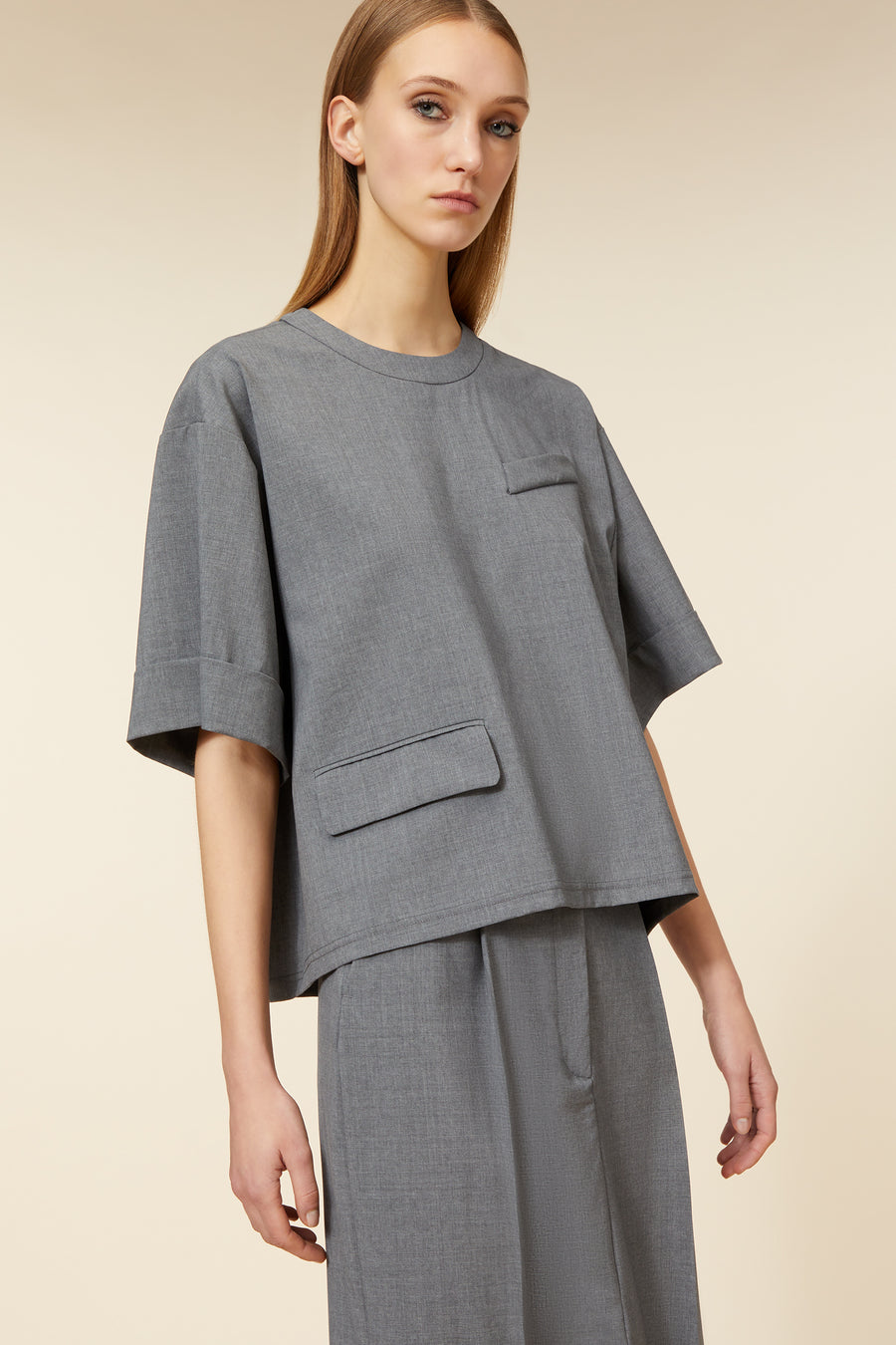 Gray tailored short-sleeved top with round neckline and patch pocket, crafted from lightweight, textured fabric for a modern look.