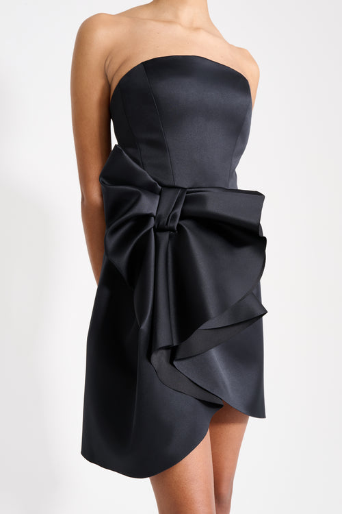 Model wearing a mini black dress on a white background.