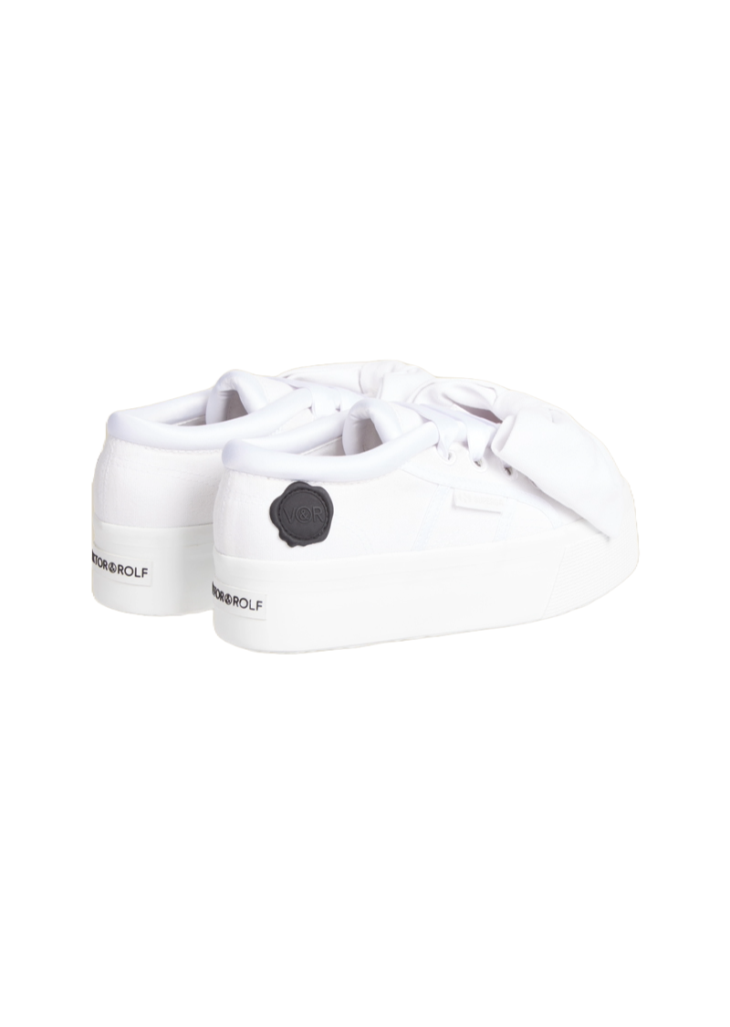 Sleek white platform sneakers feature a stylish oversized bow and embossed logo detailing on the back, embodying minimalist elegance.