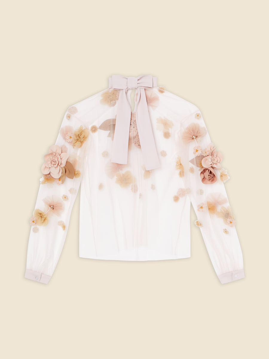 Elegant sheer blouse with delicate pink floral appliqués and long sleeves, featuring a large bow tie at the collar.