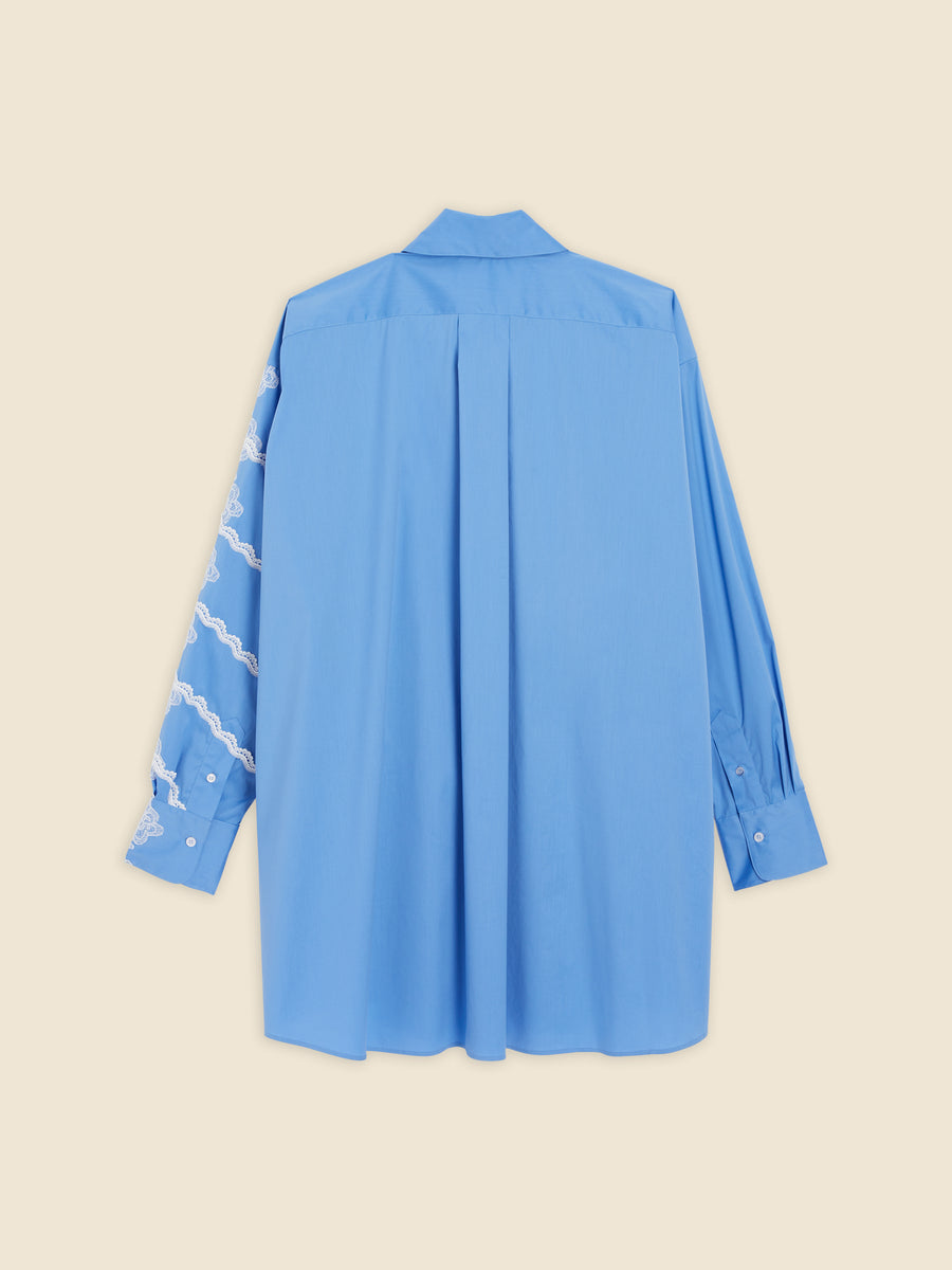 A light blue shirt featuring intricate white lace detailing on one sleeve, crafted from soft fabric for a relaxed fit.