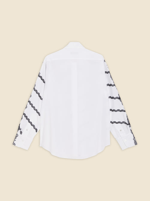 White cotton blouse with intricate black lace embroidery on long sleeves, showcasing a classic button-down design.