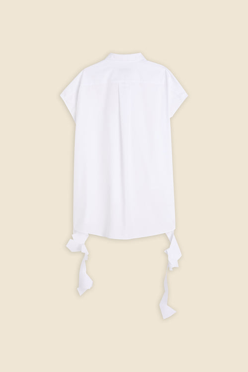 Back view of a white short-sleeve cotton blouse with decorative ribbon accents against a beige background.