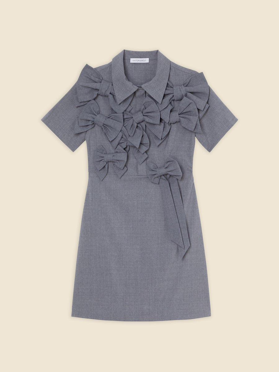Gray short-sleeved dress with oversized bow embellishments, featuring a classic collar and tailored fit, set against a beige backdrop.