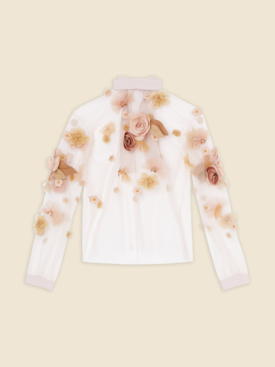 Sheer white blouse adorned with delicate peach and beige floral appliqués and long sleeves on a plain background.