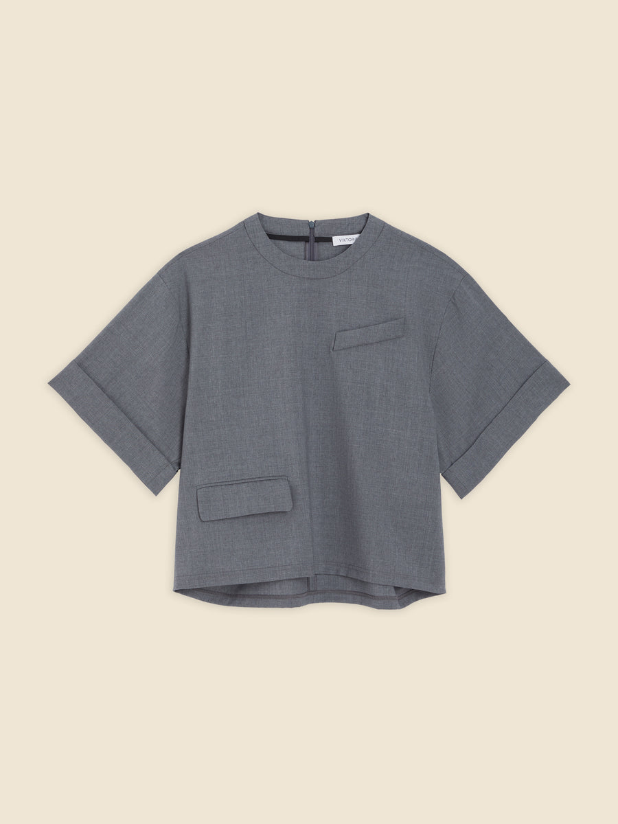 Gray linen blend top with short sleeves and minimalist pocket details, featuring a boxy silhouette and back zipper closure.