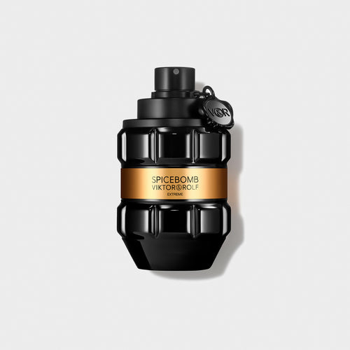 Black grenade-shaped perfume bottle with an amber label, featuring sculpted geometric facets, against a grey background.