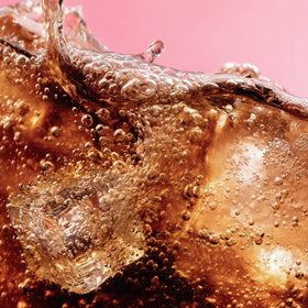Close-up of a carbonated drink with bubbles against a pink background